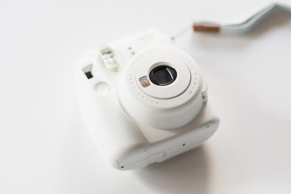 2017_0303_0081 White compact camera with lens facing upward on a white surface, strap visible in background