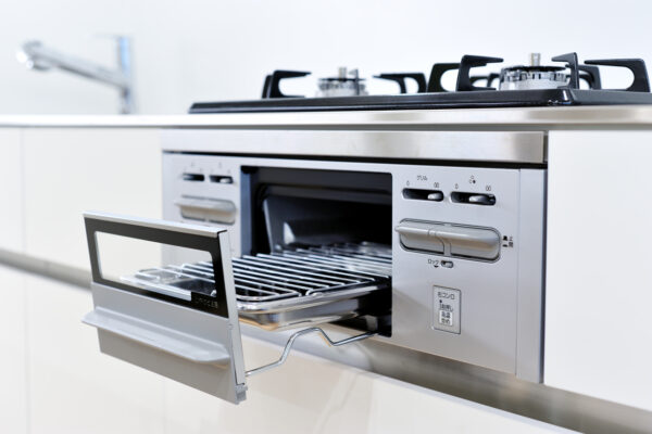 Stainless steel built-in oven with the door open, a metal rack inside, and a gas cooktop on top in a bright, modern kitchen.