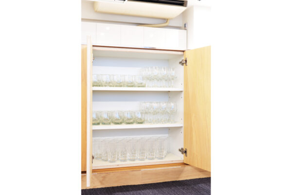 Wooden kitchen cabinet with glassware neatly arranged on three shelves (drinking glasses and stemware). Inward-opening doors are swung open for viewing the glassware inventory.