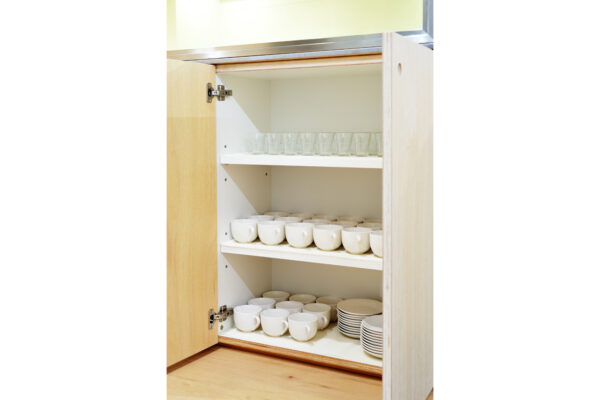 Open kitchen cabinet with three shelves holding white cups, saucers, and glassware on top shelf? (Continue)