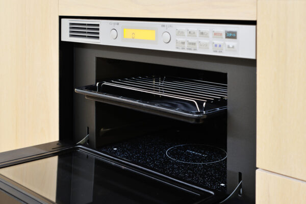 Built-in oven with door open and a pulled-out chrome rack, surrounded by light wood cabinets.