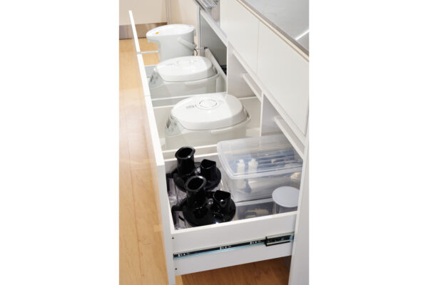 Pull-out kitchen drawer containing three white rice cookers stacked on the left and a clear plastic organizer with small items on the right.