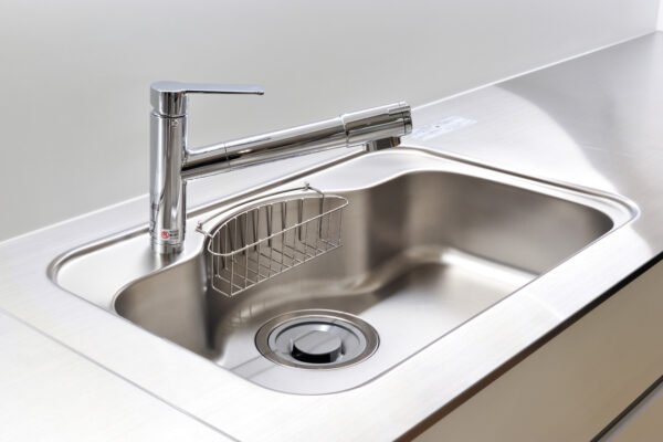Stainless steel kitchen sink with a tall lever faucet and a small wire rack mounted on the basin side.