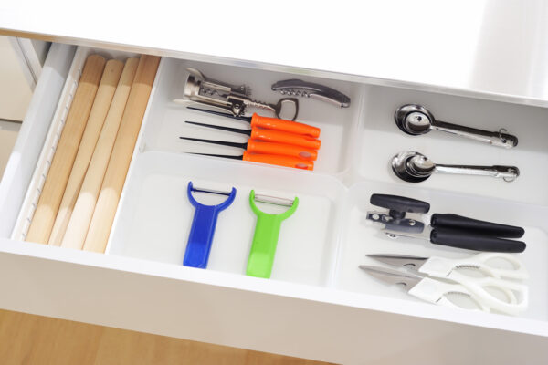 Open kitchen drawer with organized utensils: wooden cutting boards on the left and a variety of peelers, corkscrew, and can openers in the middle and right sections.