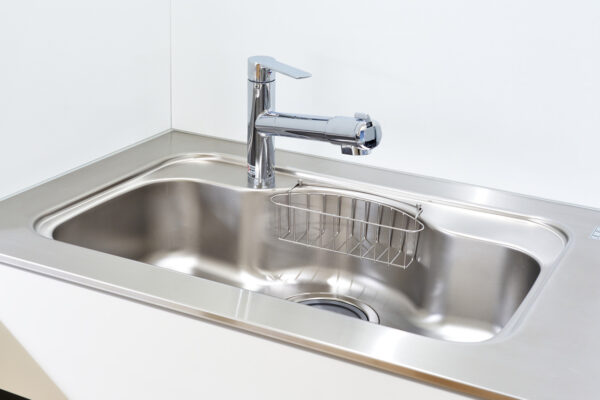 Stainless steel kitchen sink with a chrome faucet and a metal wire rack inside the basin.