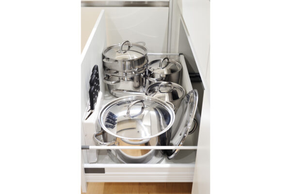Pull-out kitchen cabinet filled with shiny stainless steel pots and pans with lids.