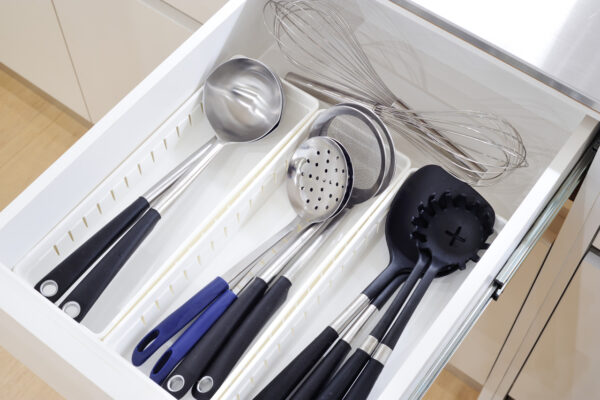 Drawer full of stainless steel and black-handled kitchen utensils: ladles, slotted spoon, colander, whisk, and spatulas neatly arranged in a divider