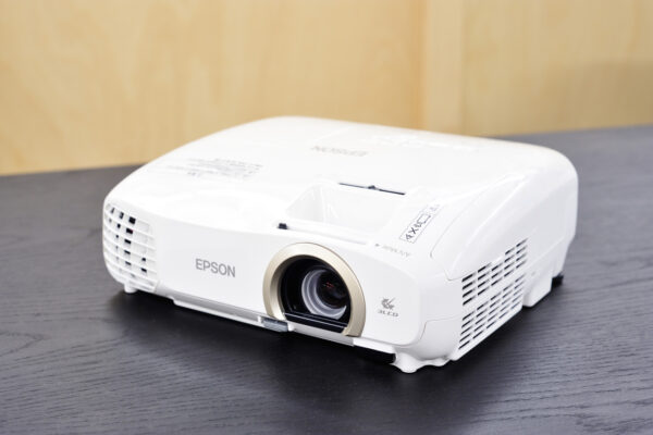 White Epson projector on a dark table, lens facing forward.