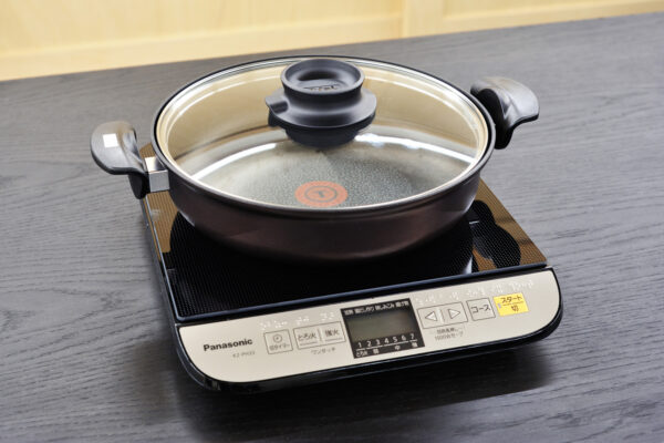 Induction cooktop in use with a glass-lidded pot ready for cooking on a dark countertop.