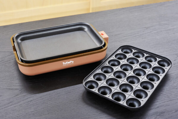 Electric takoyaki maker with a brown outer body and a removable nonstick griddle, placed on a dark wooden table.