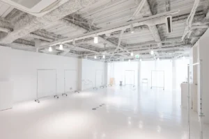 Bright minimalist photography studio with white walls, exposed ceiling, and rolling garment racks along the sides.