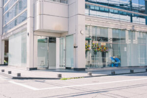 Modern glass storefront on a street, with an open door and colorful flower bouquets in the display window.