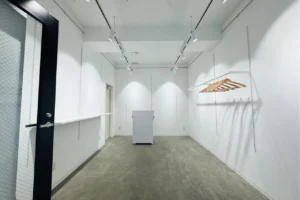Empty white showroom with track lighting, a long counter on the left, and a clothing rack on the right.