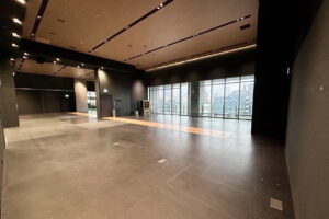 Empty modern event hall with dark walls, polished floor, and floor-to-ceiling windows overlooking a city skyline.