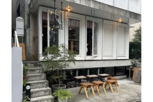 Front of a small coffee shop with large white-framed windows and wooden stools lined up outside on a concrete patio.