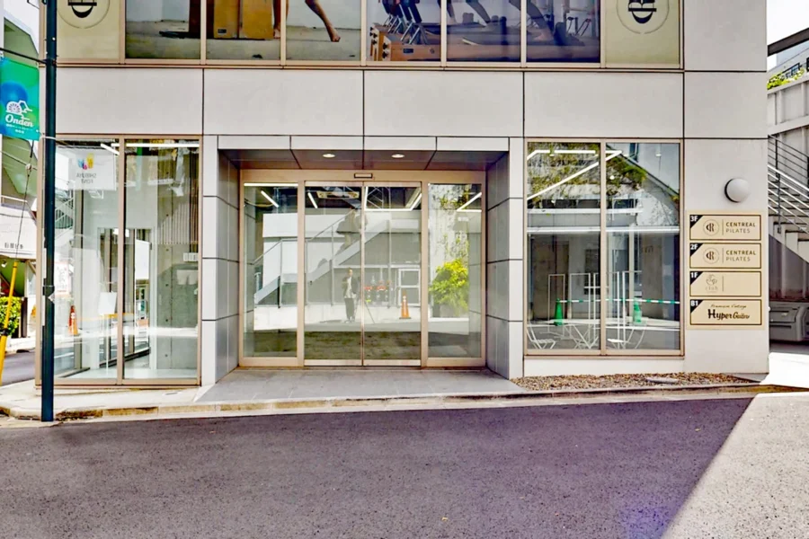 05192025_2028331 Contemporary building entrance with glass double doors and a tiled facade; signs for tenants on the right side paneling