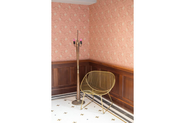 Vintage corner with pink damask wallpaper, dark wood wainscoting, a tall brass floor lamp, and a yellow wire chair in the corner.