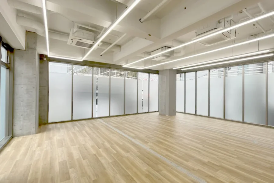 IMG_4542 Open, empty modern office space with frosted glass partitions, light wood flooring, and exposed ceiling pipes.